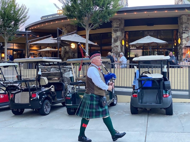 Bruce Locken playing bagpipes in kilt at golf event with carts