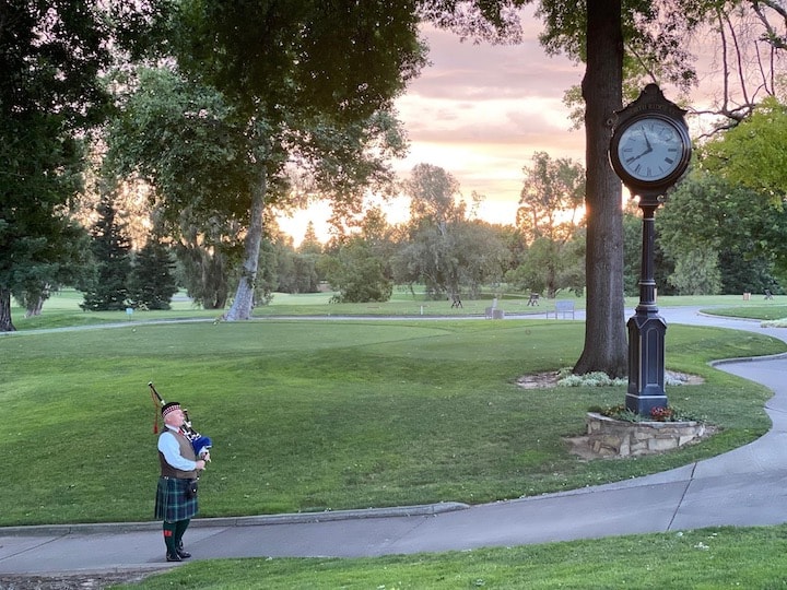 Bruce Locken playing bagpipes at sunset by a clock at a golf course