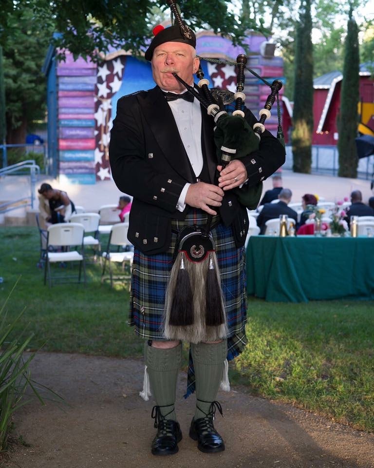Bruce Locken playing bagpipes on a neighborhood street at dusk
