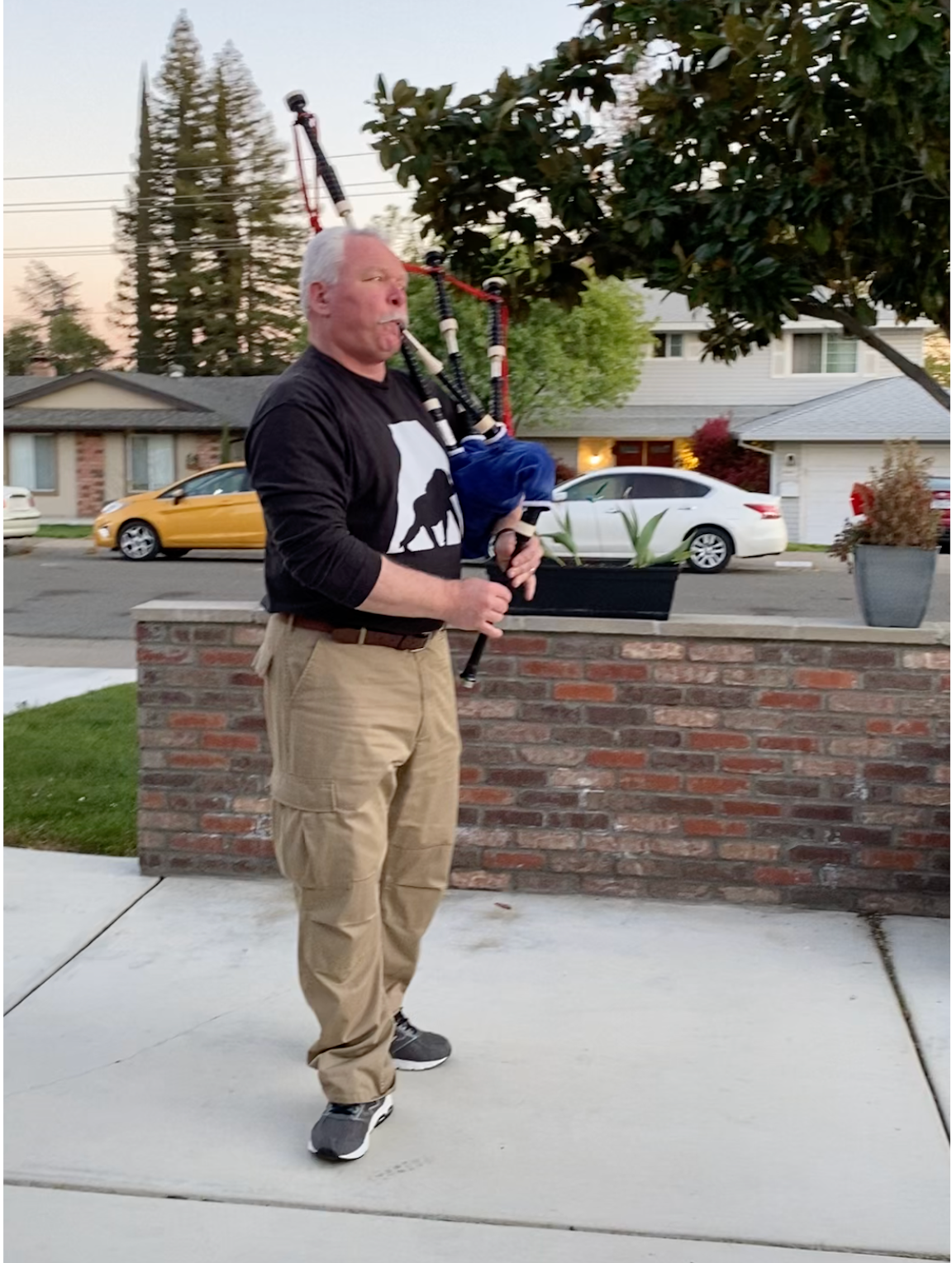 Bruce Locken playing bagpipes in formal Highland dress at outdoor event