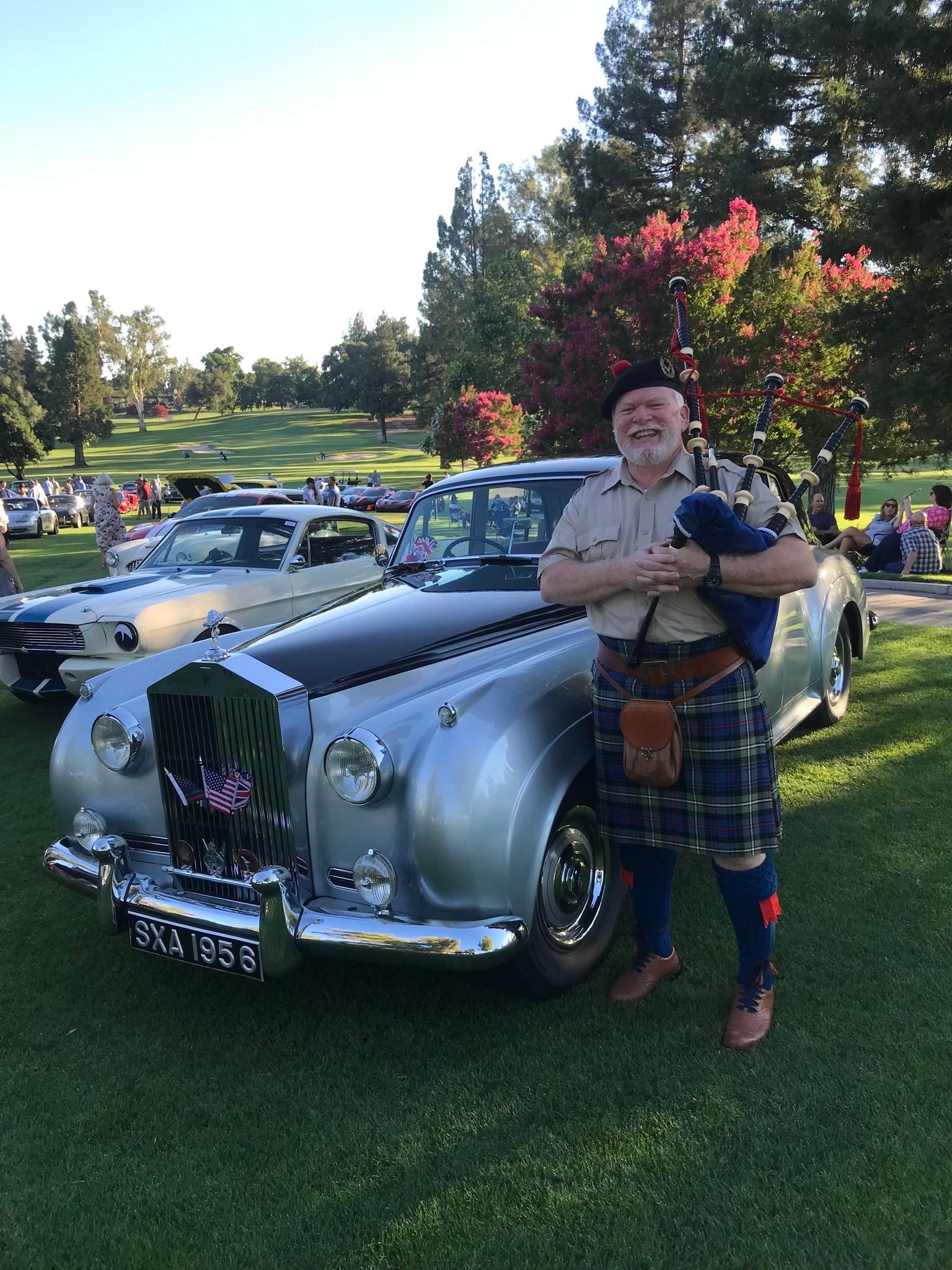 Bruce Locken smiling with bagpipes beside a classic Rolls-Royce