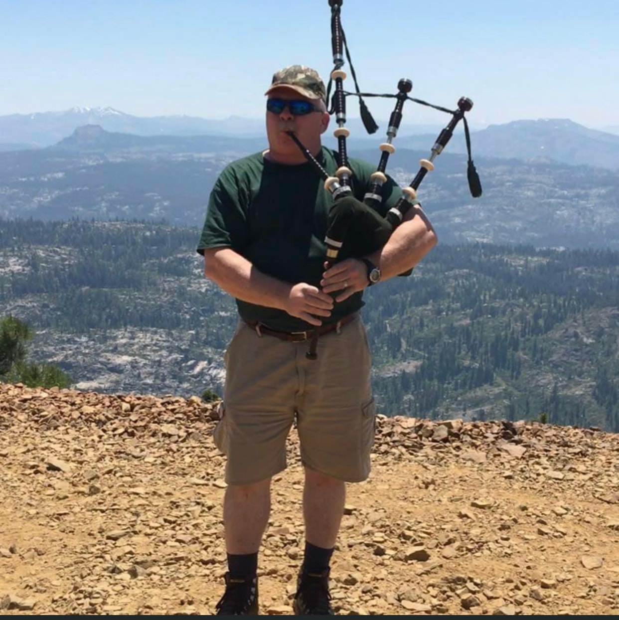 Bruce Locken playing bagpipes at Signal Peak with mountain views