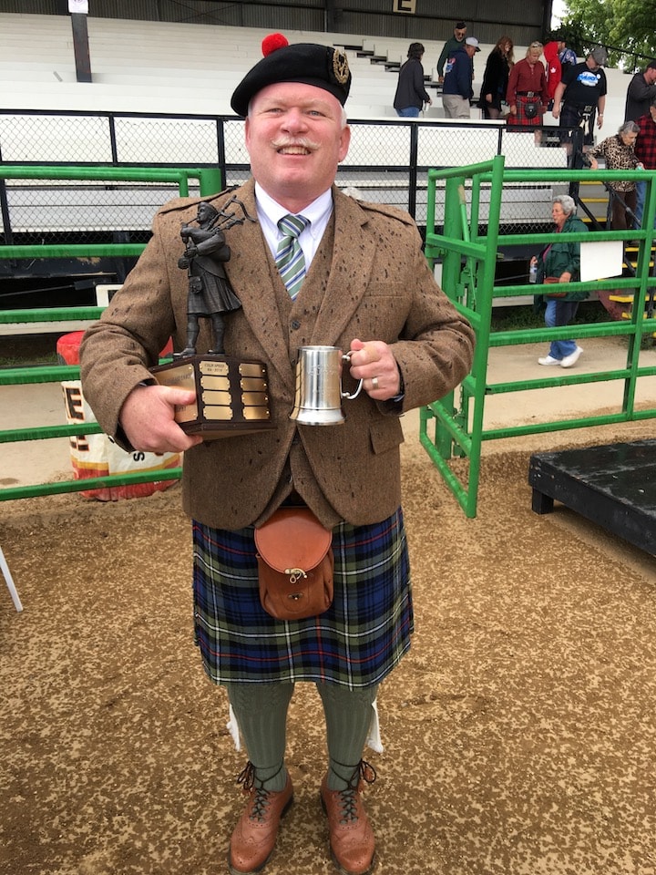 Bruce Locken in kilt holding competition trophies